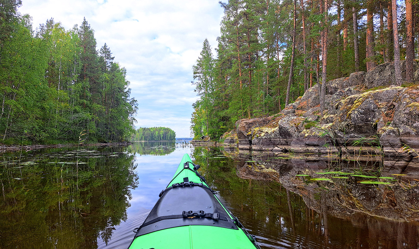 The cliffs of Aittosalmi and a glassy-calm lake beside the rocky shore; a kayak glides on the surface.