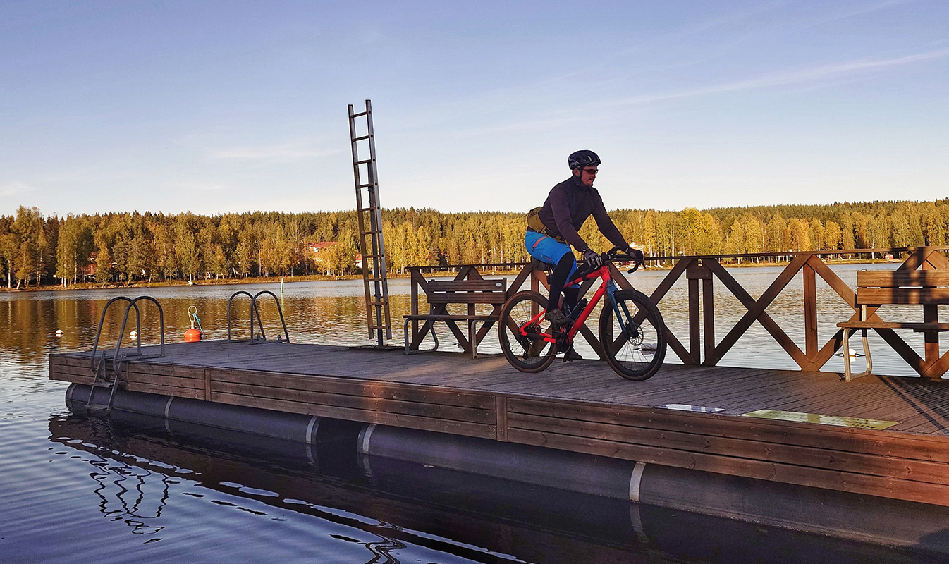 Cyclist on a pier by the lake, the forest tinted orange in the sunlight.