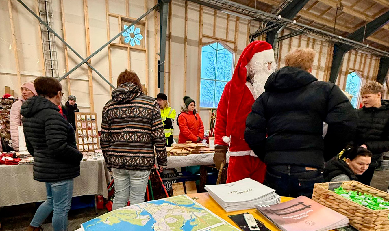 Photo of a train depot with sales tables and people. In the foreground, the project’s stand with maps and info about Äänekoski.