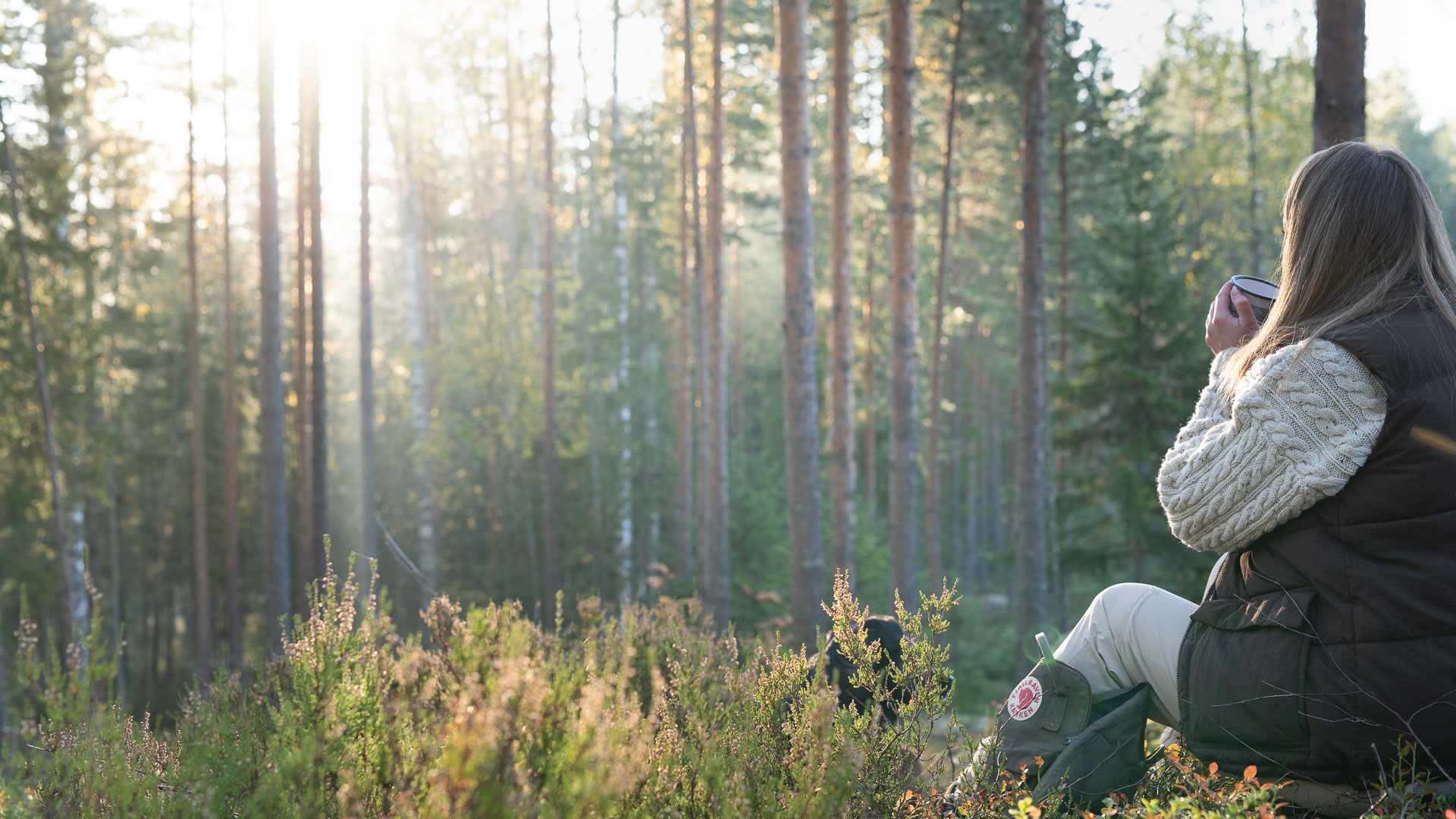 A person sits in the forest drinking something warm.