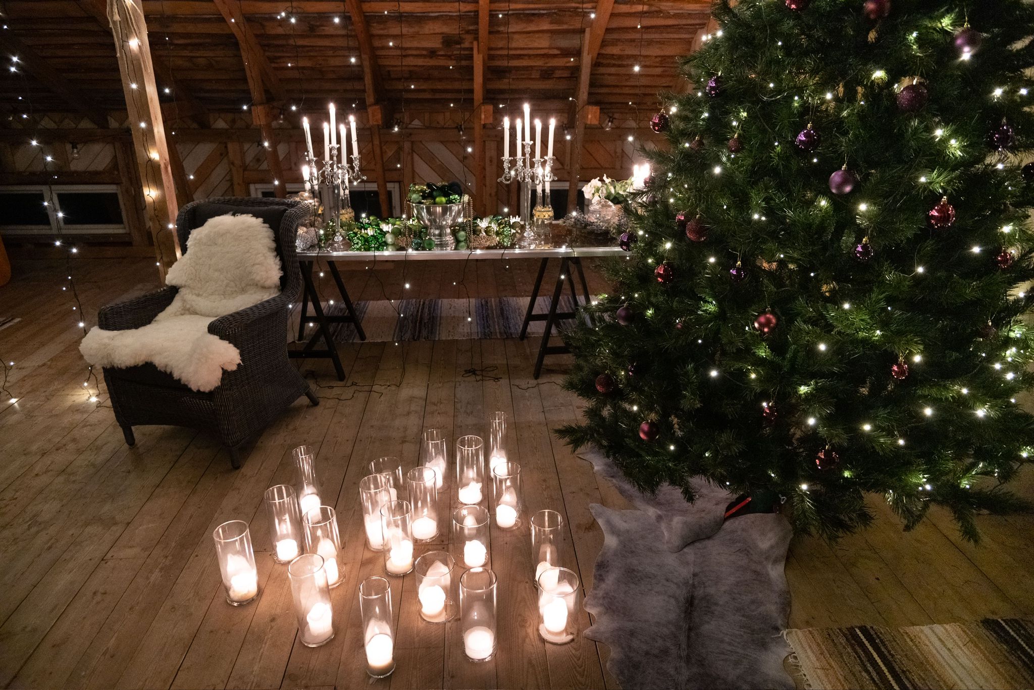 Close-up of a Christmas-decorated space. In the foreground, a chair with pillows and fabrics. Further back, a table with a tablecloth, books, and Christmas decorations.