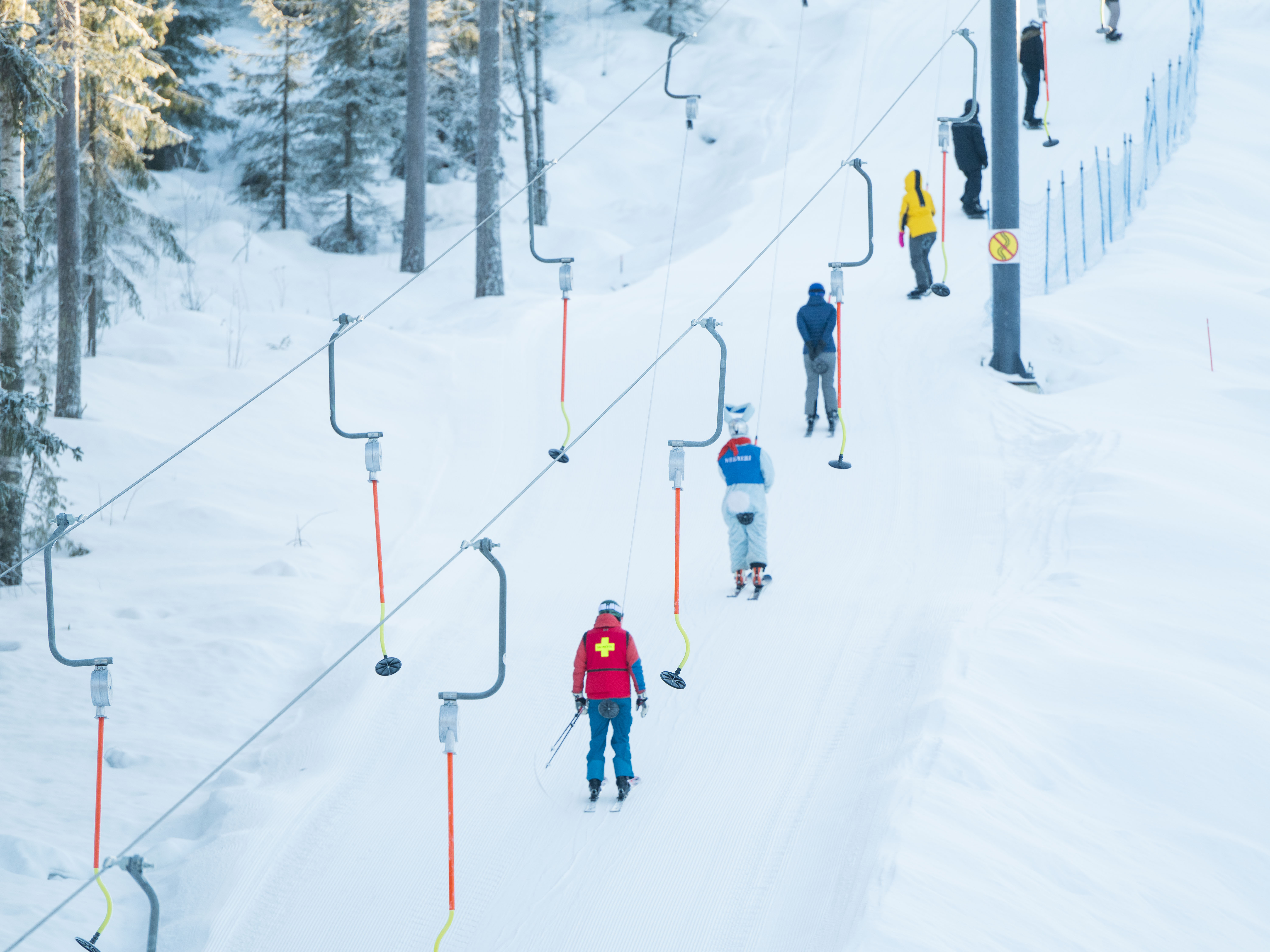 People riding a button lift on a ski slope.