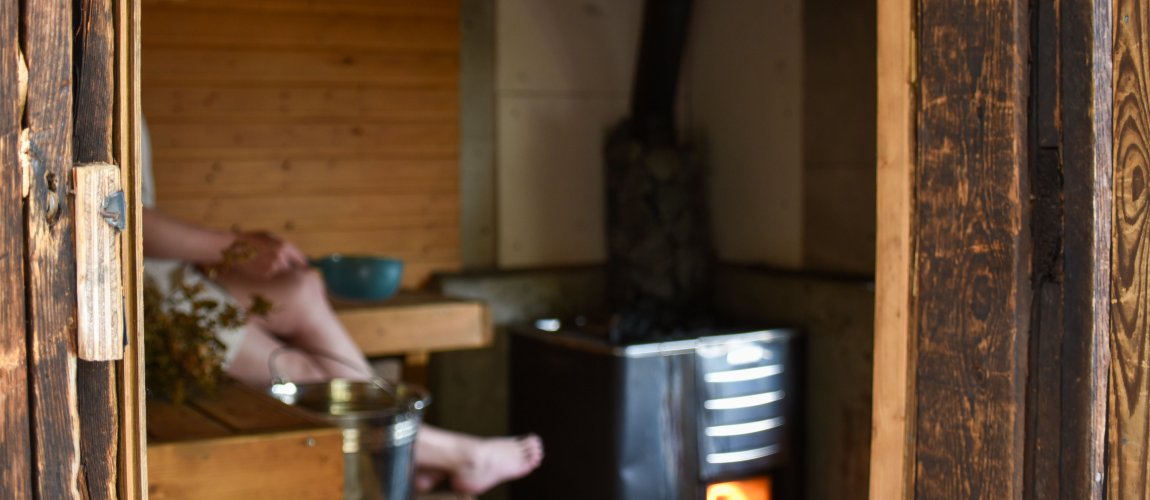 A person is sitting on the sauna benches, the stove glows with fire.