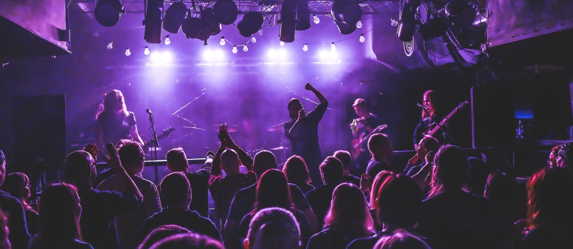 The band performs on stage and part of the audience raises their hands in the air.